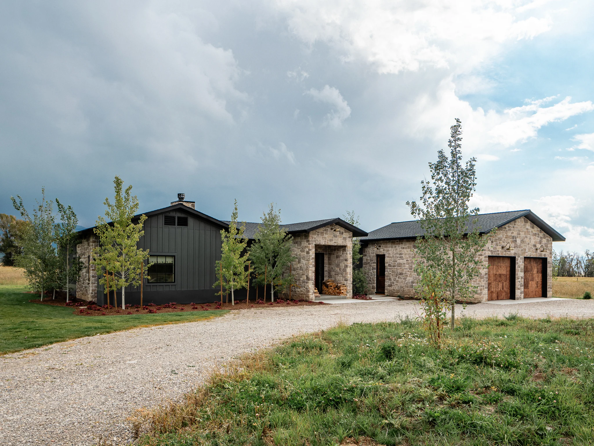 Exterior front elevation with stone and dark metal siding beneath storm clouds — architectural photography Driggs Idaho, WTG Architects
